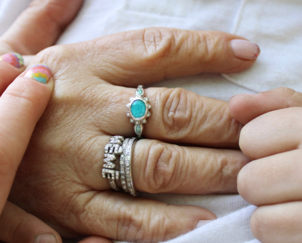 Close-up holding Grandma's hand wearing the new grandma wearing the new paraiba tourmaline flower ring and other rings