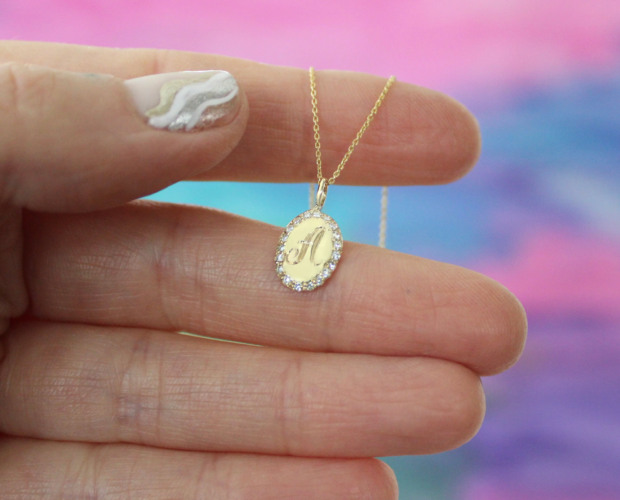 Close-up holding the Oval Charm Necklace, 14k yellow gold, diamonds