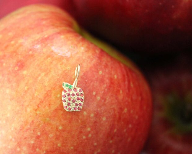 gold apple charm with red ruby gemstones on top of a ruby red apple